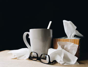 cup of tea next to a box of tissue, with scattered tissues surrounding