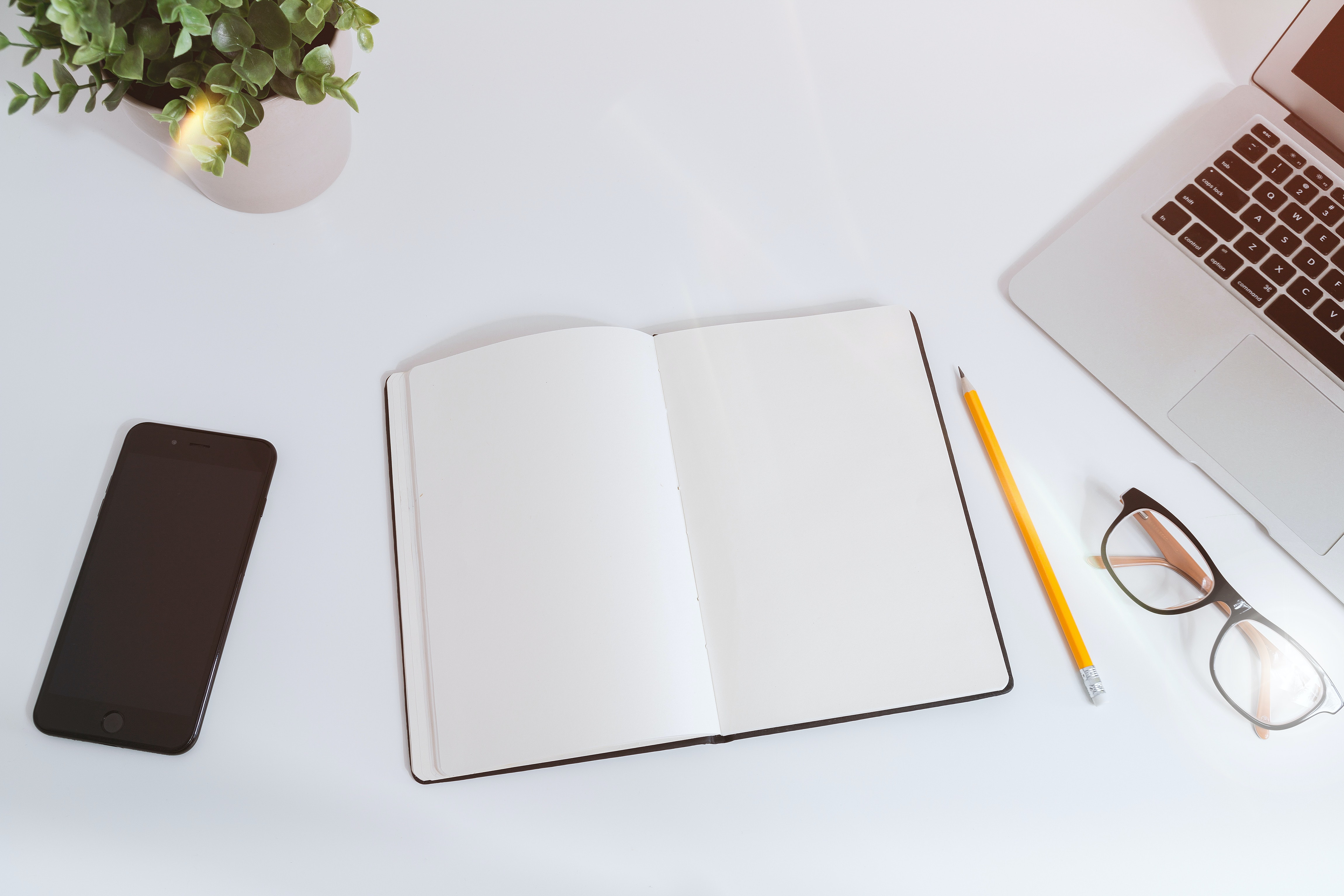 an organized desk space featuring a smart phone, notebook, glasses and a laptop