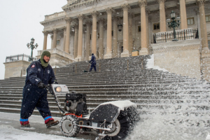 a person blowing snow with a machine in front of a Capitol Hill building